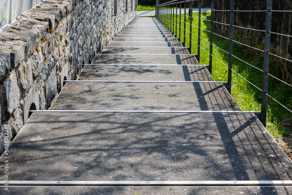 Pedestrian walkway leading down between a natural stone wall and a steel handrail