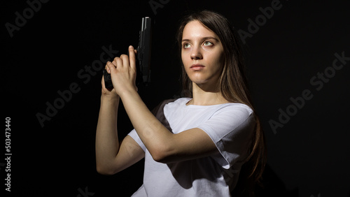 young woman with long hair in a white t-shirt with a gun on a black background