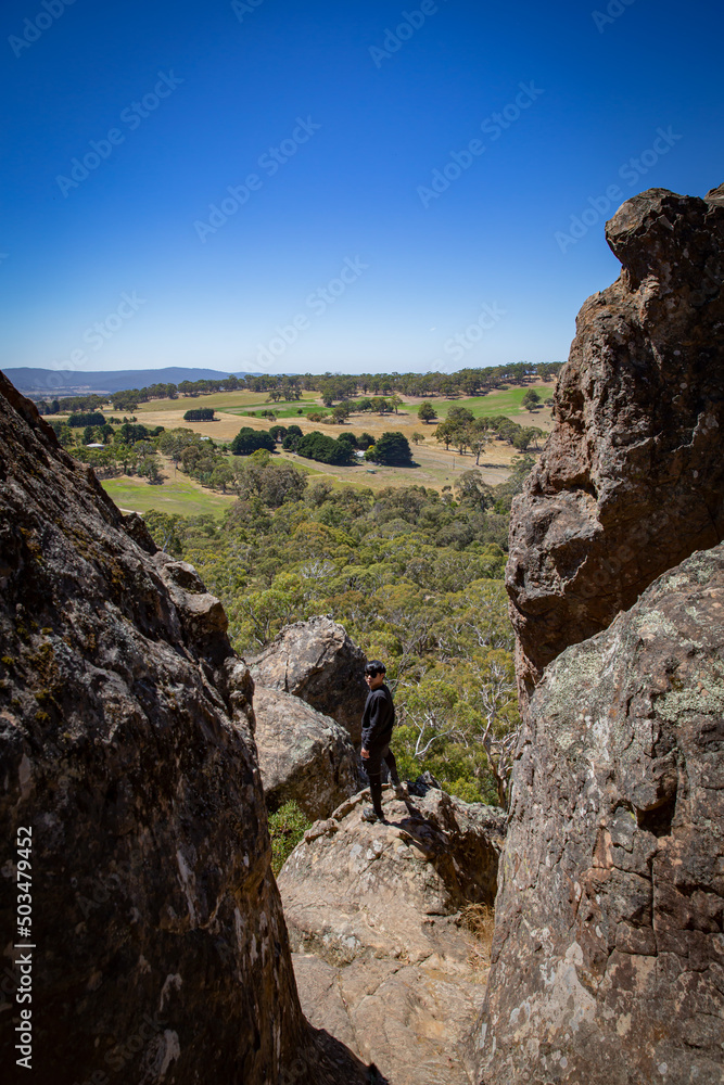 Cool man is overlooking the area from a landscape rock park Hanging Rock national park with rough stone structure and blue sky