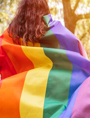 Lesbian woman wearing an LGBTQ flag, symbol for the homosexual community, as a cape. Gay rainbow colors flag for pride month and the celebration day of sexual and love diversity