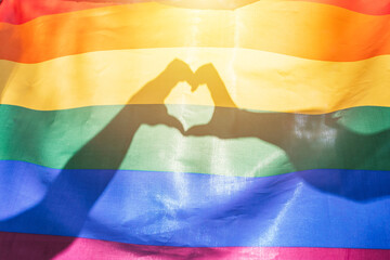 LGBTQ rainbow colors flag, a symbol for the homosexual community, two hands making a heart shape shining by sunlight. Gay flag for pride month and the celebration day of sexual and love diversity