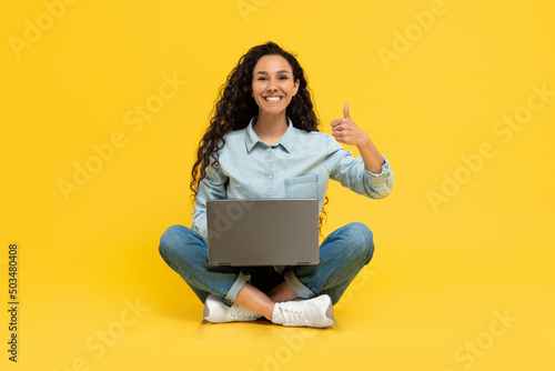 Cheerful young woman using laptop at studio showing like
