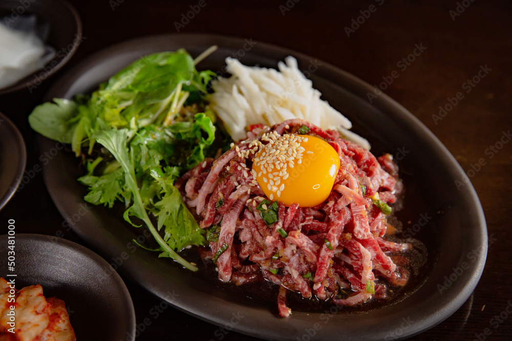 Korean Grilled BBQ combo sets with egg yolk beef tartare with pickle salad on the dark plate and black table vibe background, and pickle dishes
