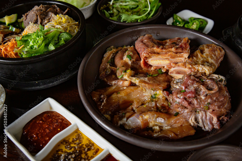 Korean Grilled BBQ combo with marinated beef pork meat set on the traditional grill table, with bibimbap, dipping sauce and pickle dishes Korean Grilled BBQ combo with marinated beef pork meat set on the traditional grill table, with bibimbap, dipping sauce and pickle dishes