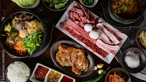 Top view of Korean Grilled BBQ combo sets on the traditional grill table, bibimbap, pork belly, wagyu and marinated chicken, rice dipping sauce and pickle dishes