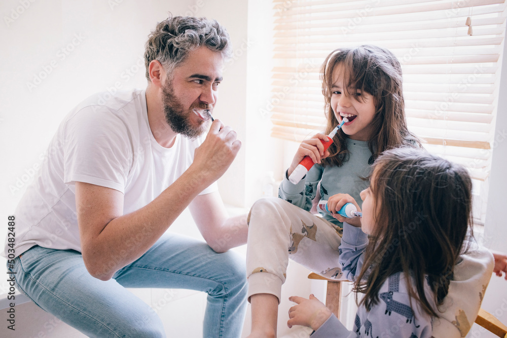 Father and daughters brushing teeth together in bathroom at home Father and daughters brushing teeth together in bathroom at home
