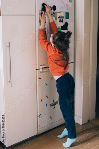 Full length of girl sticking magnet on refrigerator door at home photo