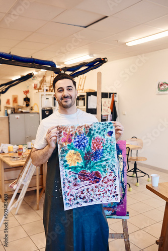 Portrait of smiling male painter showing multi colored canvas painting in art class photo