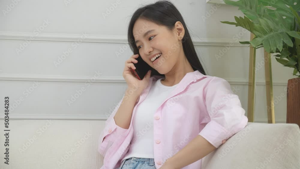 Happiness young asian woman sitting on sofa and talking with smartphone at home, female calling and speaking and listening with smart phone on couch at house, lifestyles and communication concept. Happiness young asian woman sitting on sofa and talking with smartphone at home, female calling and speaking and listening with smart phone on couch at house, lifestyles and communication concept.