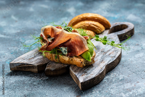 Variety of aperitifs Croissant sandwiches with jamon ham serrano paleta iberica, blue cheese, avocado, microgin on blue background Fototapet