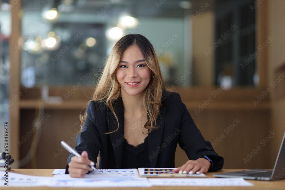 Fototapeta premium Portrait of a business woman working or secretary with laptop and financial documents on the desk in the office. Looking at camera.