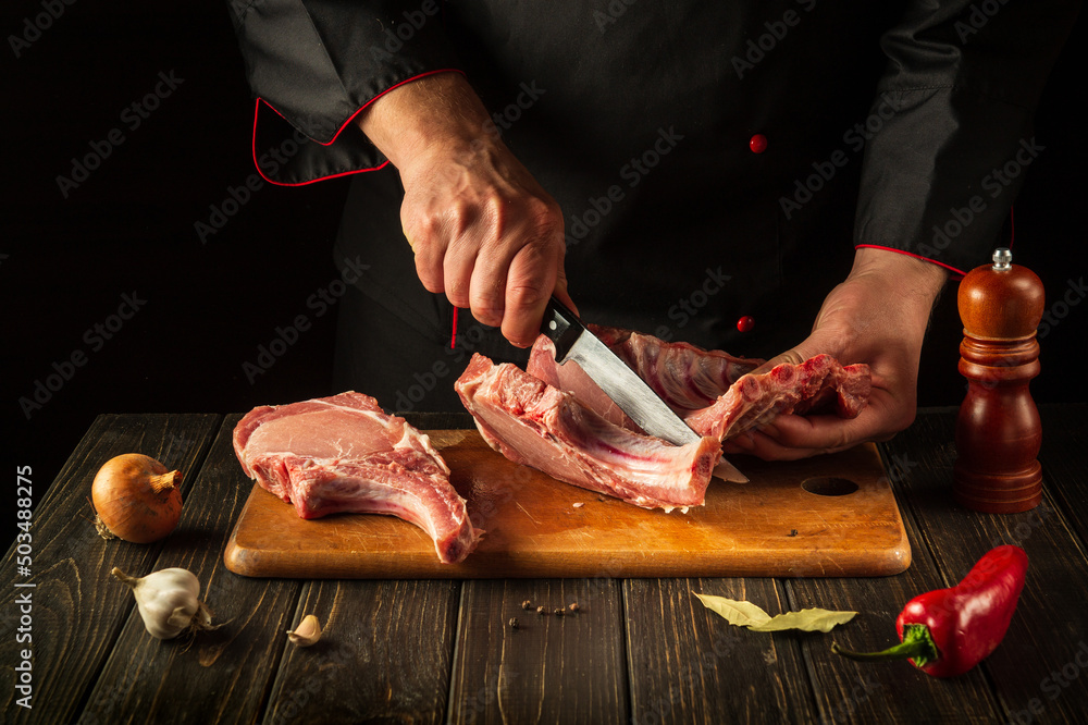 Butcher cuts raw ribs on a cutting board before grilling. European cuisine. Meat dish idea for a hotel