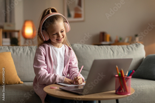 Happy Girl Using Laptop Taking Notes Wearing Earphones At Home