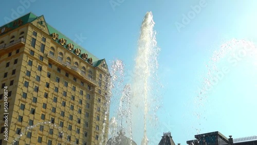 High fountains on square of Europe in Batumi Against background of blue sky. Fountain beats upwards against background of large tall building. Adjara. Large number of jets of foda soar into air. photo