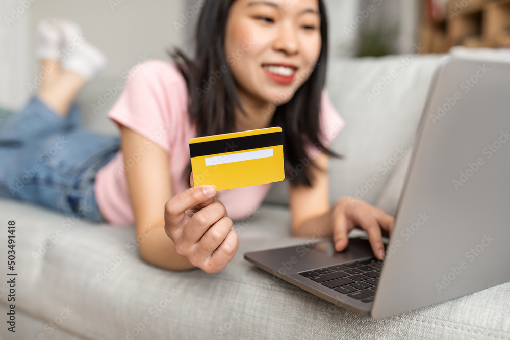 Online shopping concept. Asian lady with laptop and credit card making purchases in web store from home, selective focus Online shopping concept. Asian lady with laptop and credit card making purchases in web store from home, selective focus