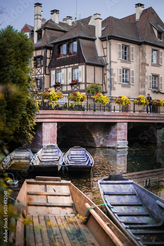 weathered boats in the river against historical wooden architecture with shutters of the Alsace town in a dusk