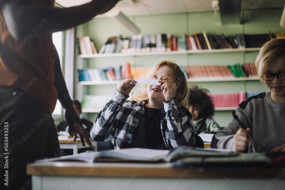 Boy showing paper chit to teacher while copying in classroom Boy showing paper chit to teacher while copying in classroom