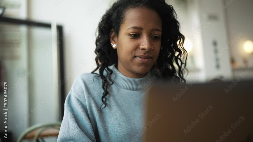 Happy African woman wearing blue sweater typing by laptop in cafe Happy African woman wearing blue sweater typing by laptop in cafe