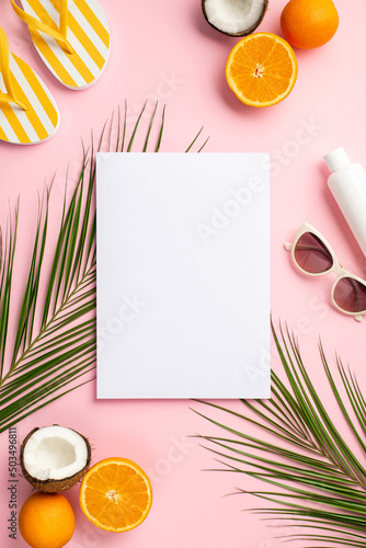 Summer concept. Top view vertical photo of paper card sunglasses sunscreen tube yellow slippers coconuts oranges and palm leaves on isolated pastel pink background with blank space