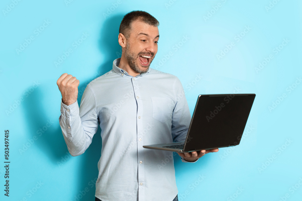 Middle Aged Man Holding Laptop Computer Gesturing Yes, Blue Background Middle Aged Man Holding Laptop Computer Gesturing Yes, Blue Background