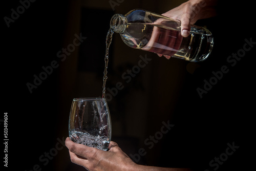 delicate woman's hand holding a bottle of water, pouring water in a glass, black background, concept of vitality, health, wellness