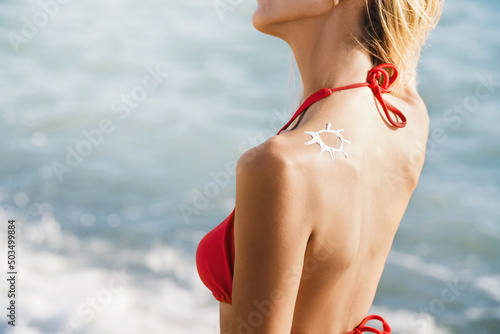 Woman apply sunscreen on skin and tanning on the beach. A sun painted on the skin by cream