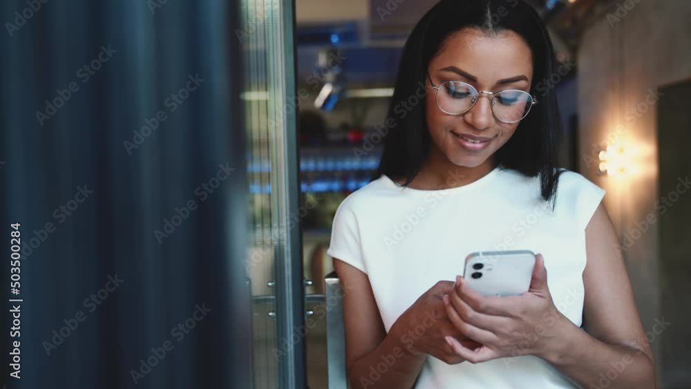 Positive African woman texting by mobile in cafe