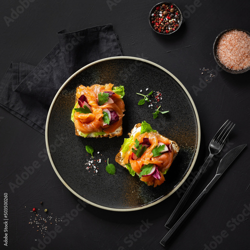 Smorrebrod - traditional Danish sandwiches. Black rye bread with salmon, cream cheese, capers on black background. Top view photo