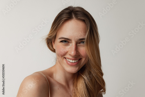 Portrait of tender young woman with perfect face smiling at camera, posing isolated over grey studio background