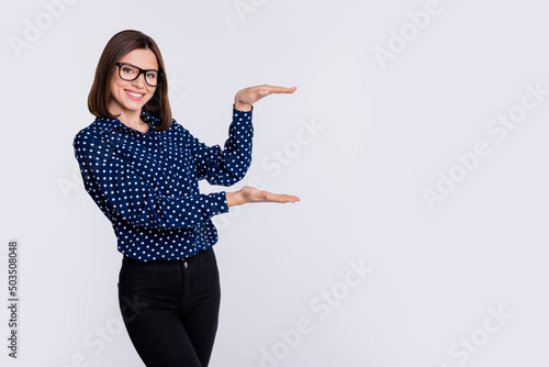 Portrait of attractive cheerful girl demonstrating size gift surprise copy space isolated over grey pastel color background