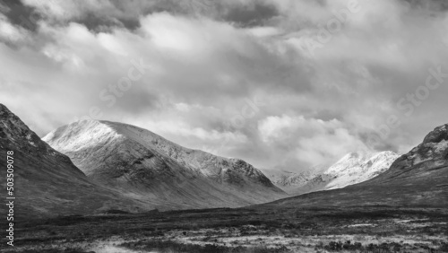 Black and white Majestic beautiful Winter landscape image of Lost Valley in Scotland with snowcapped Buachaile Etive Baeg sand distant mountain range with dramatic sky photo
