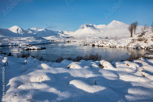 Beautiful Winter landscape image looking towards Scottish Highlands mountain range across Loch Ba on Rannoch Moor