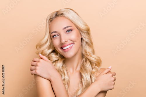 Portrait of attractive cheery wavy-haired girl touching smooth shoulders fresh shower isolated over beige pastel color background