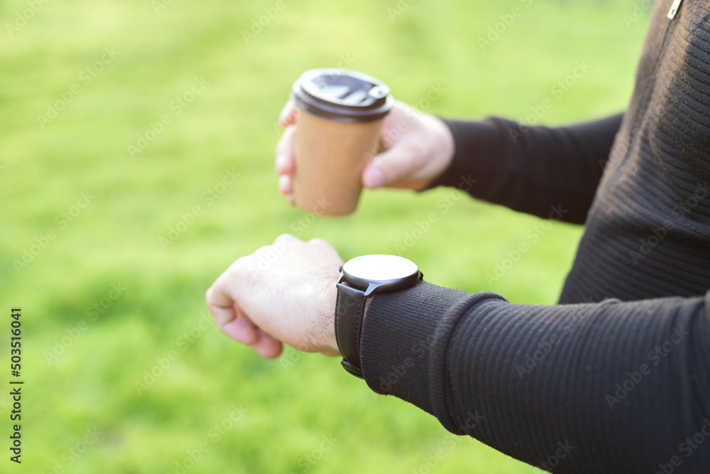 the man looks at the mockup of the hand watch. in the hand of a craft cup on a green background the man looks at the mockup of the hand watch. in the hand of a craft cup on a green background