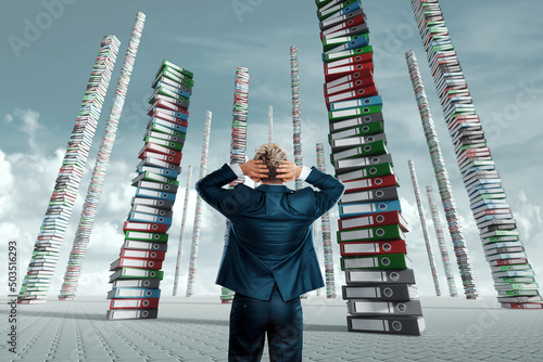 Papier peint An unhappy office worker, a businessman, looks at the towers from many folders with documents