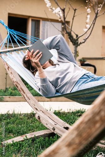Mature woman in a hammock on a lawn on the lawn reading an e-book