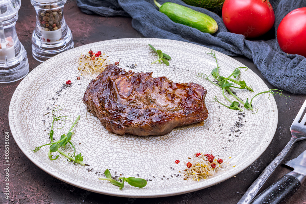 juicy Ribeye steak on grey plate on dark stone table