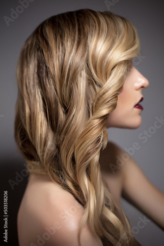 Profile Sexy Blond Fashion Model Posing with Perfect Long Curly Hair in Studio on Grey Background