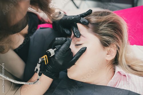Cosmetologist applying permanent make up eyebrows for a client