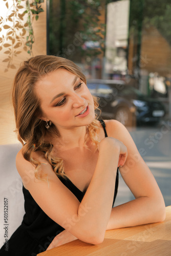 A young businesswoman communicates with someone sitting at a table, behind the glass of the street