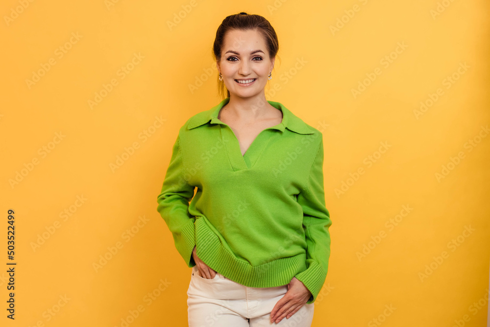 Beautiful young woman in a green jacket on a yellow background smiles happily, looks into the camera Beautiful young woman in a green jacket on a yellow background smiles happily, looks into the camera