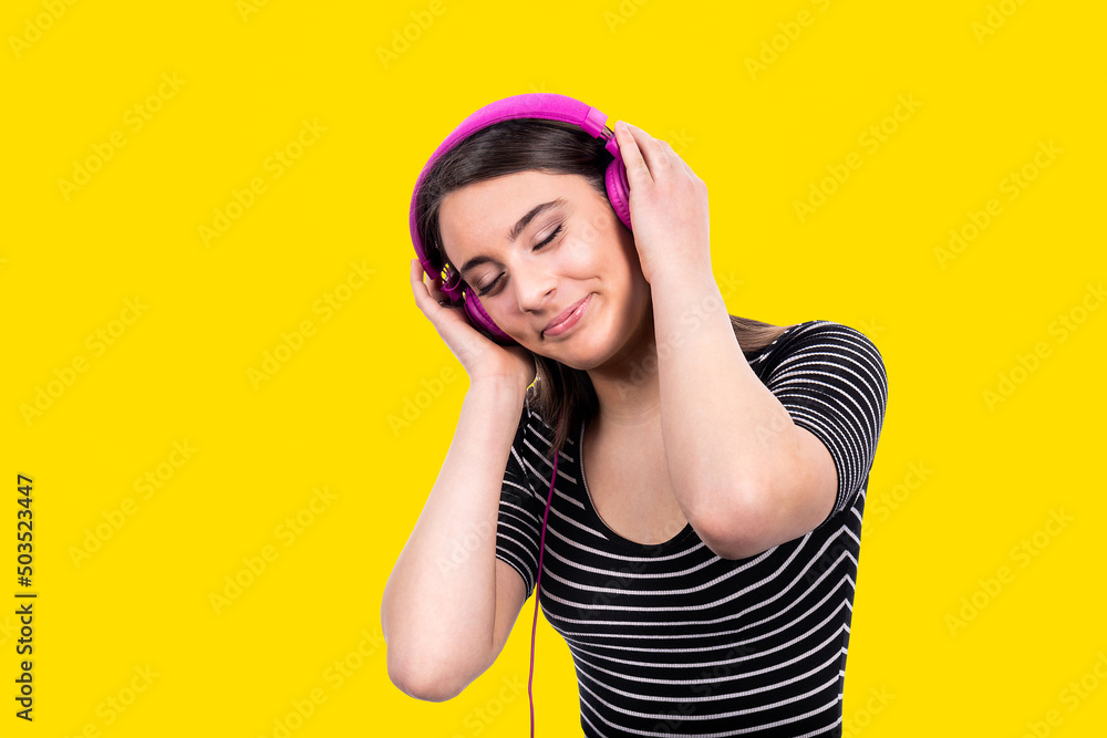 Obraz premium Portrait of beautiful smiling girl with long hair. The young woman wears jeans and a striped shirt and uses headphones to listen to music.