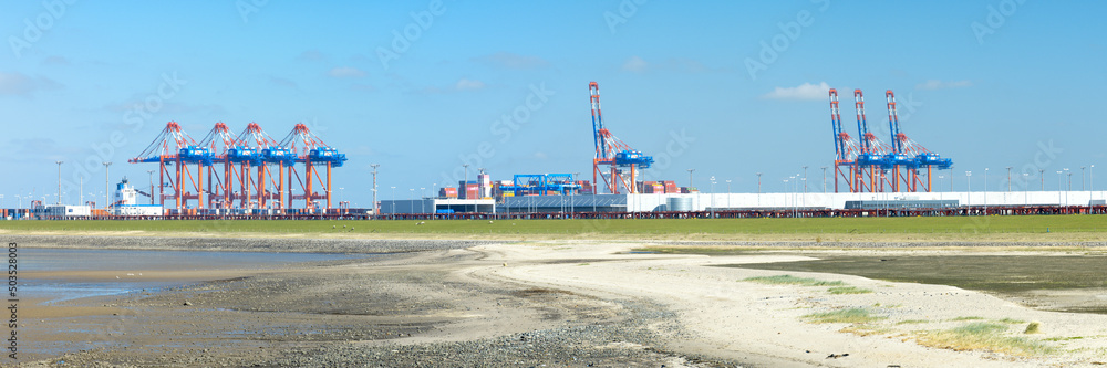Panorama of container gantry cranes with industrial halls at the Jade Weser Port, deep water harbor in Germany.