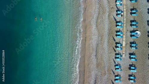 Two lonely tourists swimming in the sea in the sunny morning along the empty beach with sun loungers in Oludeniz Turkey photo