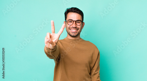 young handsome hicpanic man smiling and looking friendly, showing number two or second with hand forward, counting down