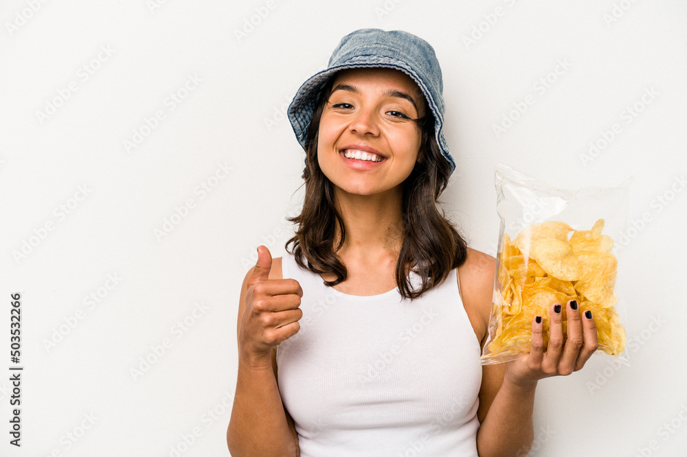 Young hispanic woman holding a bag of chips isolated on white background smiling and raising thumb up Young hispanic woman holding a bag of chips isolated on white background smiling and raising thumb up