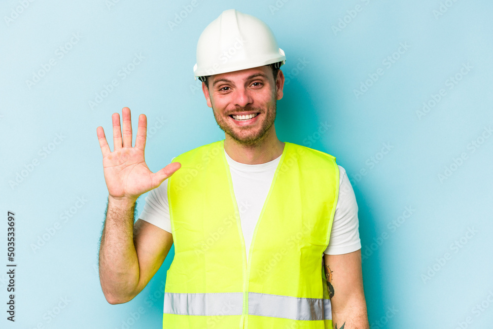 Young laborer caucasian man isolated on blue background smiling cheerful showing number five with fingers.