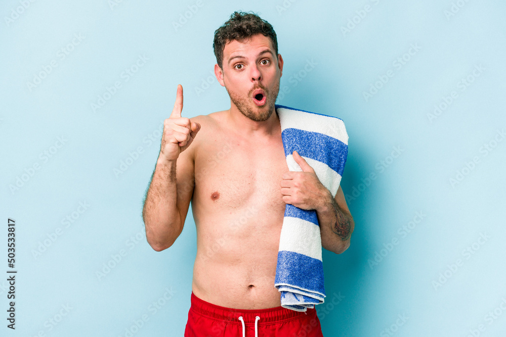 Young caucasian man holding beach towel isolated on blue background having some great idea, concept of creativity.