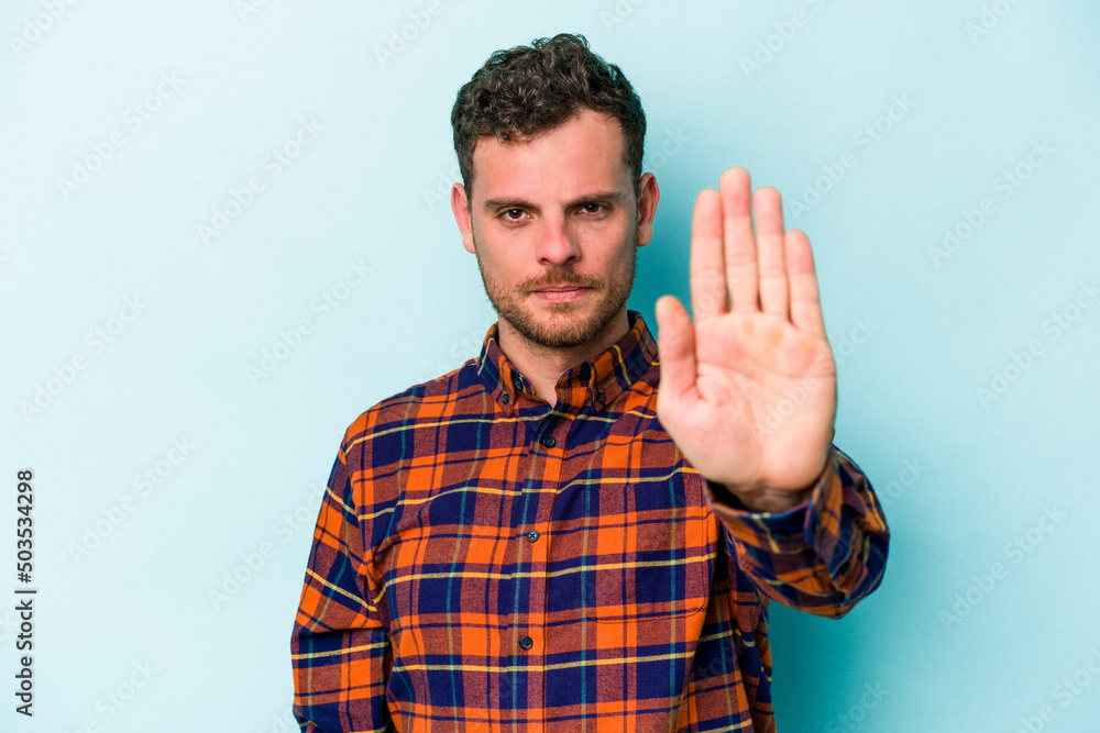 Young caucasian man isolated on blue background standing with outstretched hand showing stop sign, preventing you. Young caucasian man isolated on blue background standing with outstretched hand showing stop sign, preventing you.
