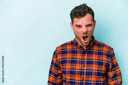 Young caucasian man isolated on blue background shouting very angry, rage concept, frustrated.